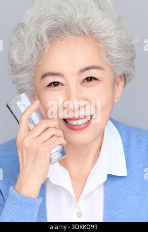 Fröhliche ältere asiatische Frau mit kurzen silbernen Haaren in blauer Strickjacke, die Glück und gesunden Lebensstil zum Ausdruck bringt, Studio-Porträt auf einem weißen bac Stockfoto