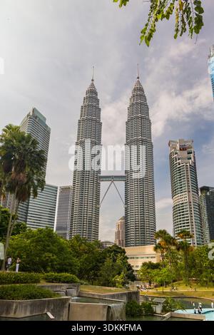 Legendäre zwei Wolkenkratzer und eine Skybridge überragt über urbanen Wasserspielen im Park Stockfoto