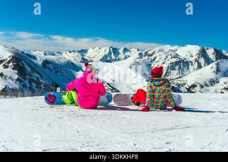 Zwei Snowboarder ruhen auf einem Berghang mit Panoramablick auf die schneebedeckten Pyrenäen bei El Tarter, Grandvalira, Andorra Stockfoto