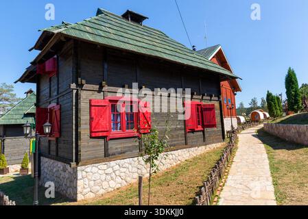Zlatibor, Serbien – 14. August 2021: Traditionelles Holzhaus mit roten Fensterläden im Cowboydorf, Teil des thematischen Touristenkomplexes auf dem Berg Zlatibor. Stockfoto