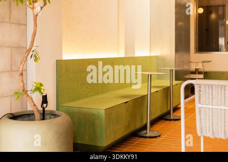 In einem hellen Café schaffen grüne Sitzplätze und kleine Tische einen einfachen und einladenden Bereich. Eine kleine Pflanze verleiht dem Design des sp. Einen Hauch von Natur Stockfoto
