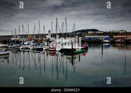 Yachten und Masten spiegeln sich im stillen Wasser eines Hafens mit Leuchtturm und entfernten Hotels an der Küste, Scarborough, North Yorkshire. Stockfoto