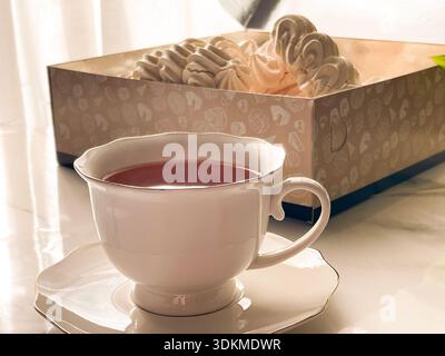 Tee mit Zephyr Marshmallows. Gemütliche Teezeit mit einer Tasse heißem schwarzem Tee und weichen, luftigen russischen zephyr Marshmallows auf einem Leuchttisch in der Nähe des Fensters. Stockfoto