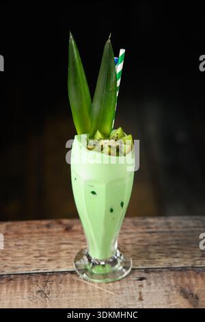 Ein grünes Getränk mit einer Ananas drauf. Das Getränk ist in einem hohen Glas und hat einen Strohhalm Stockfoto