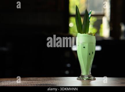 Ein grünes Getränk in einem Glas mit grünem Stroh. Das Getränk liegt auf einem Tisch Stockfoto