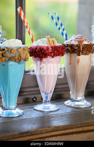 Drei Milchshakes mit verschiedenen Geschmacksrichtungen und bunten Strohhalmen. Die Milchshakes werden in hohen Gläsern mit einem blauen, rosa und braunen Milchshake serviert Stockfoto