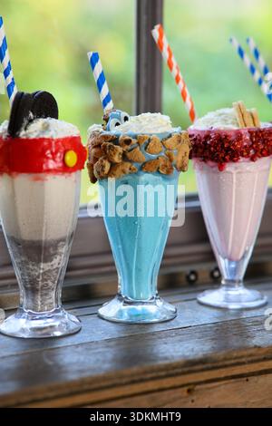 Drei Milchshakes in verschiedenen Farben mit Strohhalmen. Der blaue hat einen Keks drauf Stockfoto