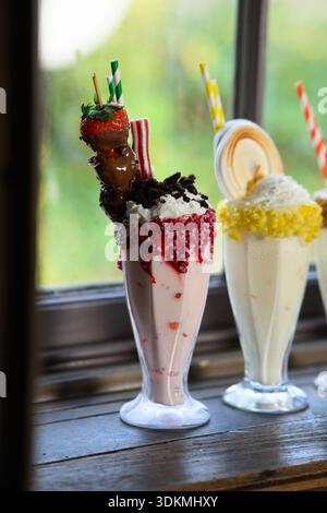 Ein köstlicher Erdbeermilkshake mit einem Spieß darauf, garniert mit einer Erdbeere und einem Schokoladenstreuer. Der Milchshake wird in einem hohen Glas serviert Stockfoto