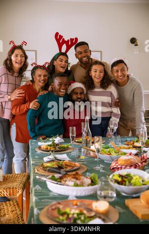 Eine große Familie steht zu Hause am Esstisch und trägt Weihnachtskopfbekleidung mit gebratenem truthahn und Salaten. Festlich, feierlich, Zweisamkeit, Wärme, multikulturell, Haushalt, fröhlich || Modell veröffentlicht Stockfoto