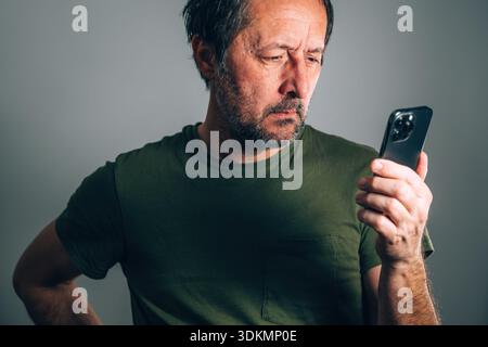 Dunkle emotionale Nahaufnahme eines erwachsenen Mannes, der auf den Bildschirm eines Mobiltelefons blickt und Sorgen, Unsicherheit und ernsthafte Gedanken bei minimalem Licht zum Ausdruck bringt Stockfoto