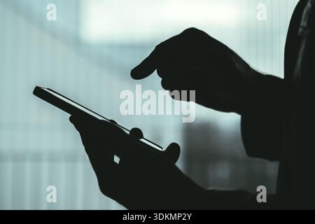 Silhouette männlicher Hände mit Smartphone in Innenräumen, anonymes Profil, das Privatsphäre, Technologienutzung, Kommunikation oder digitale Abhängigkeit zum Ausdruck bringt. Auswahl Stockfoto