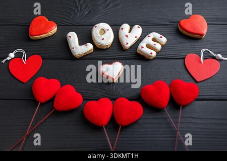 Kekse mit Liebe und roten Herzen. Dekorative Kekse mit der Schreibweise „LIEBE“ mit Herzformen und leuchtend roten Herzornamenten auf einem schwarzen Stockfoto