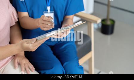 Eine Frau in blauer Uniform sitzt auf einem Stuhl mit einem Klemmbrett vor sich Stockfoto