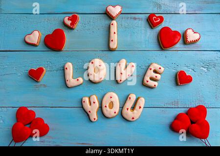 Herzförmige Kekse mit der Schreibweise „I love you“ auf blauem Holzhintergrund. Stockfoto