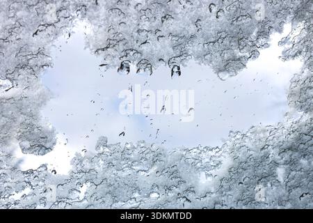 Schmelzender Schnee und Eis enthüllen einen klaren Himmel. Nahaufnahme von schmelzendem Schnee und Eis auf einer durchsichtigen Oberfläche mit Wassertropfen, die einen Teil davon umrahmen Stockfoto