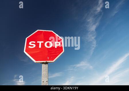 Ein leuchtendes rotes achteckiges Stoppschild steht deutlich vor einem tiefblauen Himmel mit dünnen, schimmernden weißen Wolken in Spanien, was eine klare Anweisung dazu gibt Stockfoto