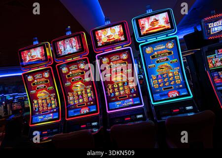 Beleuchtete Spielautomaten in einer Reihe mit farbenfrohen Spielwänden, leuchtender Neonbeleuchtung, gepolsterten Stühlen und detaillierten elektronischen Spieledisplays Stockfoto
