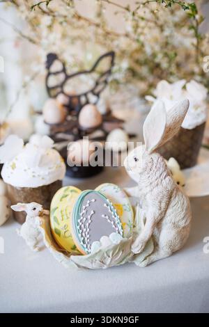 Osterkekse und Kaninchenfiguren auf dem Frühlingstisch mit Kuchen und Eiern, sanftes Licht Stockfoto