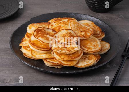 Stapel Pfannkuchen, serviert auf einem schwarzen Teller in einer gemütlichen Küche während des Frühstücks Stockfoto