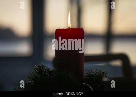 Eine einzelne rote Kerze in einem Adventskranz brennt in der Abenddämmerung vor einem Fenster und schafft eine gemütliche Atmosphäre, Finnland Stockfoto