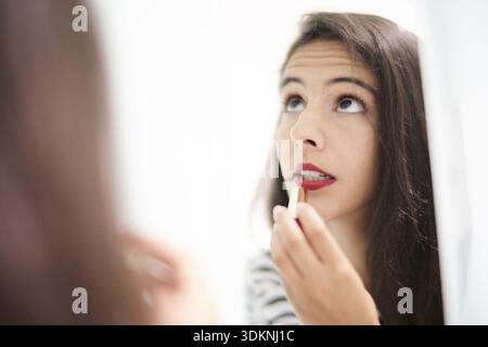 Lippenstickerei, fokussierte Frau trägt roten Lippenstift auf ihre Reflexion in Nahaufnahme, schminkt sich auf und macht sich Sorgen über schädliche Substanzen Stockfoto