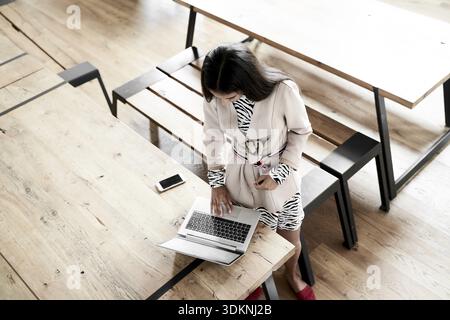 Eine Frau steht an einem Holztisch in einem öffentlichen Raum, einem Café, einer Herberge oder einem Hotel oder einem öffentlichen Raum, in dem sie aufstehen und loslegen kann Stockfoto
