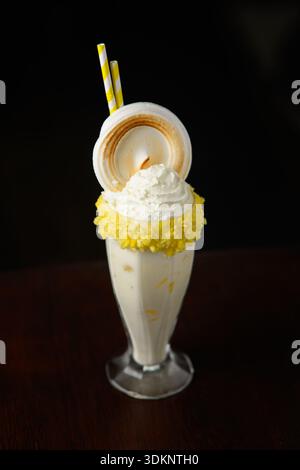 Ein Glas Eis mit gelbem Belag. Das Eis wird mit einem gelben Zuckerguss und einem Stück Kuchen belegt Stockfoto