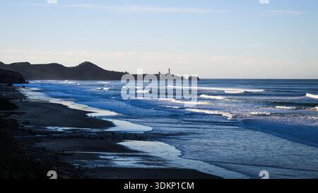 Wellen Rollen mit weißer Brandung auf einen ruhigen, einsamen Strand mit einem entfernten Leuchtturm Stockfoto