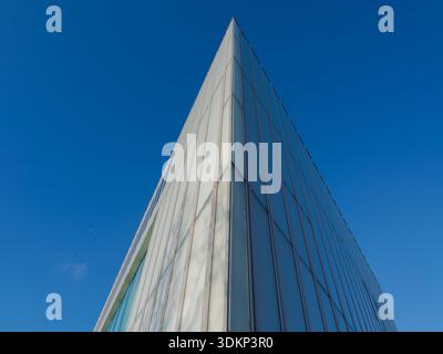 Dramatischer Blick auf ein Glashochhaus, das eine scharfe geometrische Ecke vor einem tiefblauen Himmel bildet. Moderner Architekturhintergrund mit Co Stockfoto