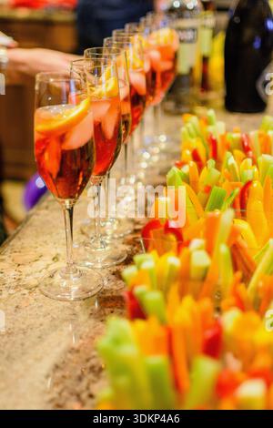 Gläser prickelnder Feiertagsgetränke garniert mit Orangenscheiben, serviert zusammen mit frischen Gemüsevorspeisen während einer Thanksgiving-Versammlung. Stockfoto