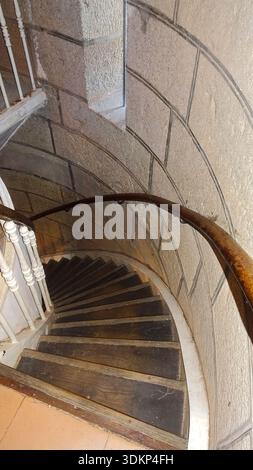 Blick von oben auf eine spiralförmige Holztreppe, die sich entlang einer Steinmauer schlängelt und ein auffälliges geometrisches Muster erzeugt. Stockfoto