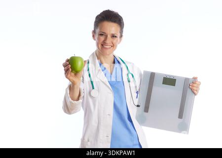 Eine Ärztin hält einen grünen Apfel und eine digitale Skala, die die Balance zwischen gesunder Ernährung und Gewichtsmanagement für Long-te repräsentiert Stockfoto
