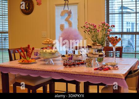 Geburtstagstisch im Prinzessin-Stil, dekoriert mit rosa und violetten Desserts, Kuchen, Obstplatten und festlicher Dekoration in einem Familienhaus. Stockfoto