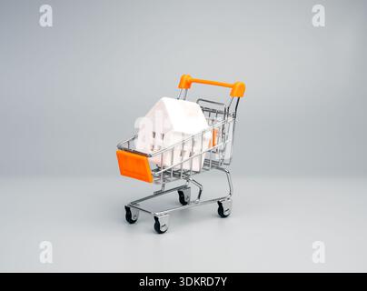 Mini-Einkaufswagen mit Hausmodell symbolisiert Immobilienkauf, Immobilieninvestition, Immobilienwert, Immobilienmarkttrends, steuerliche Auswirkungen, Hypothek, Stockfoto