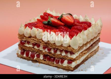 Ein optisch ansprechender, quadratischer Kuchen mit knusprigem Blätterteig, weißer Creme, rotem Beerenkompott und frischen Erdbeeren. Stockfoto