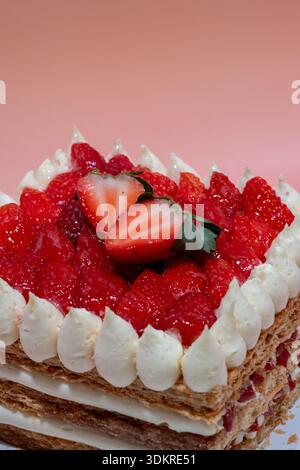 Bei einer Nahaufnahme wird ein quadratisches Dessert mit knusprigem Gebäck, Sahne und reichlich frischen Erdbeeren aufgenommen, garniert mit halbierten Beeren und Sahne Stockfoto
