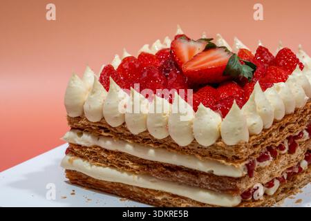 Ein Gourmet-Erdbeer-Mille-Feuille-Kuchen mit knusprigem Gebäck und Sahne, garniert mit frischen Erdbeeren, präsentiert auf einem weißen Teller. Stockfoto