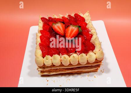 Ein quadratischer Erdbeer-Mille-Feuille-Kuchen mit blättrigen Teigschichten, frischen Beeren und Paspelcreme steht auf einer weißen Tafel. Stockfoto