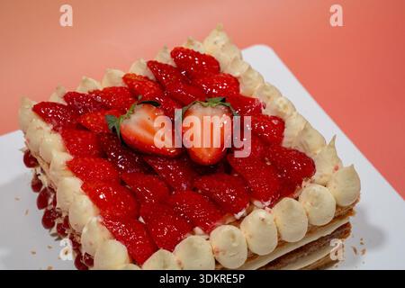 Ein frisch gebackener Erdbeerkuchen, garniert mit glasierten Beeren und Sahne, liegt auf einem weißen Teller. Stockfoto