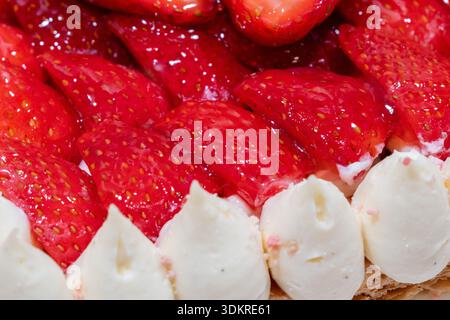 Eine Nahaufnahme eines Erdbeerdesserts zeigt leuchtend rote glasierte Beeren, weiße Paspelcreme und eine knusprige Teigbasis. Stockfoto