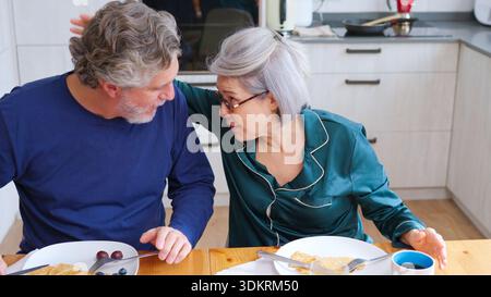 Seniorenpaar, das sich während des Frühstücks im Pyjama zu Hause unterhält Stockfoto