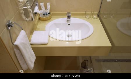 Sauberer Kosmetikbereich im Bad mit Waschbecken, Chromarmatur, frischen weißen Handtüchern und kostenlosen Toilettenartikeln Stockfoto