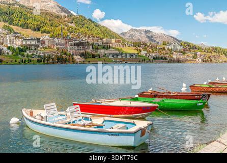 Ruderboote legen an einem klaren sonnigen Tag am St. Moritzsee mit Bergstadt und Bergkulisse im Engadin an. Stockfoto