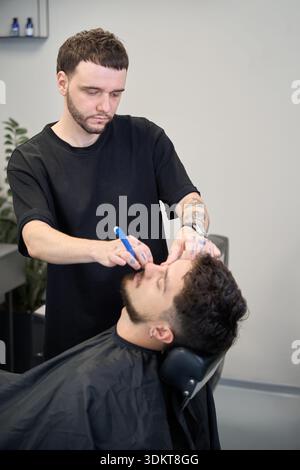 Der Gesichtspflege schneidet den Bart mit einem scharfen Rasierer Stockfoto