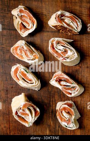 Köstliche Lachsräder mit Frischkäse-Kräutern auf hölzernem Hintergrund. Gourmet-Vorspeisen mit geräuchertem Lachs, Weichkäse, Füllung mit gewickeltem Tortil Stockfoto