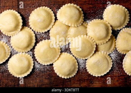 Handgemachte Ravioli Pasta auf bemehltem Holzschneidebrett. Traditionelle italienische Küche mit rohen Teigtaschen, die zum Kochen bereit sind. Stockfoto