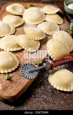 Frische hausgemachte Ravioli Pasta auf Holzschneidebrett mit Nudelschneider, mit Mehl bestäubt für die traditionelle italienische Zubereitung Stockfoto
