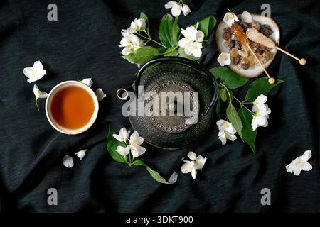 Traditionelle Teezeremonie mit gusseiserner Teekanne Tasse Tee Jasminblüten und natürlichen Zutaten auf dunklem Stoffhintergrund Stockfoto