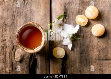 Keramik-Teetasse auf rustikalem Holztisch, dekoriert mit weißen Jasminblüten und traditionellen asiatischen Süßigkeiten Mochi-Kugeln von oben Stockfoto