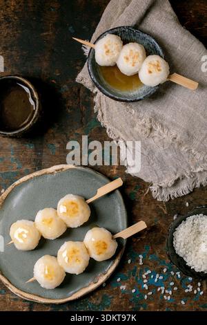 Traditionelle japanische Dangoknödel auf Spießen, serviert auf Keramikplatten mit Tee. Süße Reiskugeln auf rustikalem hölzernem Hintergrund mit Leinen cl Stockfoto